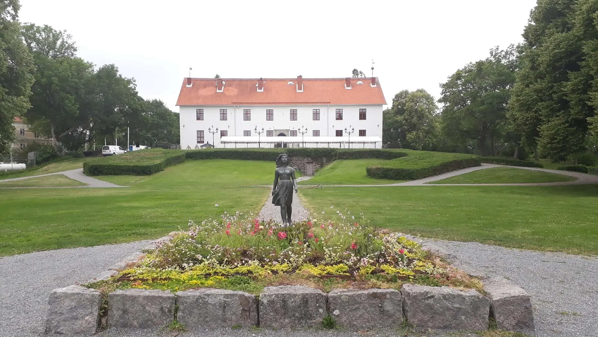 Blommor och staty med gräsmatta och vit slottsbyggnad i bakgrunden.